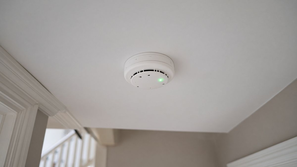 A white round smoke alarm with a green indicator light on a landing ceiling