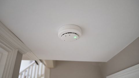 A white round smoke alarm with a green indicator light on a landing ceiling